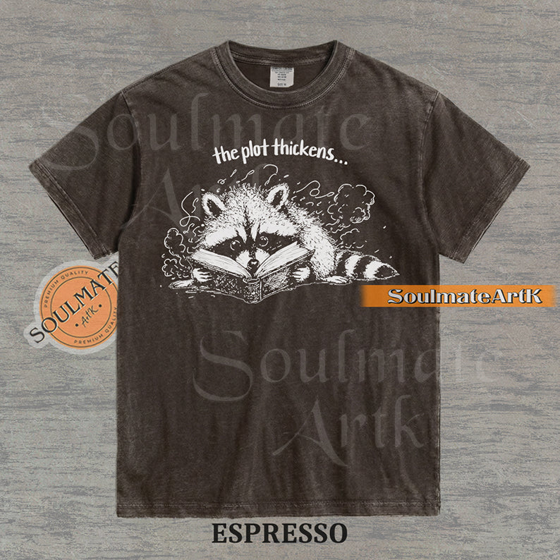Hand-drawn black and white illustration of a raccoon reading a book with the text The Plot Thickens on a vintage t-shirt