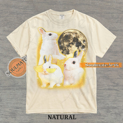 Graphic of three white rabbits—one wearing yellow sunglasses—next to a full moon in a golden space setting on a natural t-shirt.