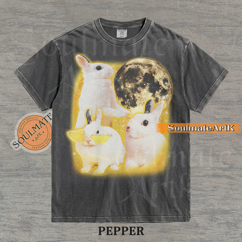 Graphic of three white rabbits—one wearing yellow sunglasses—next to a full moon in a golden space setting on a washed pepper t-shirt.