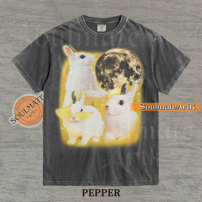Graphic of three white rabbits—one wearing yellow sunglasses—next to a full moon in a golden space setting on a washed pepper t-shirt.