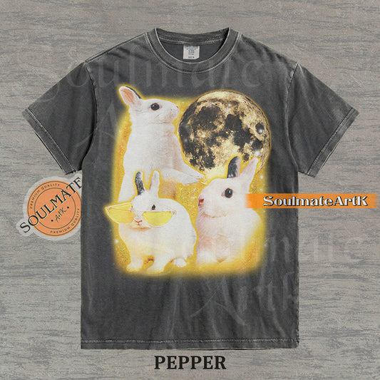 Graphic of three white rabbits—one wearing yellow sunglasses—next to a full moon in a golden space setting on a washed pepper t-shirt.