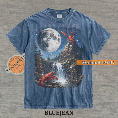 Graphic of crawfish on a mountain peak and by a waterfall under a giant full moon on a washed bluejean shirt.