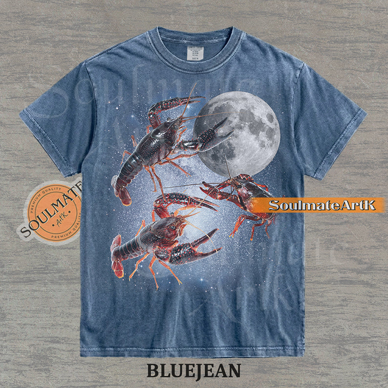 Graphic of three crawfish floating in a starry space nebula next to a full moon on a washed bluejean shirt.