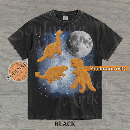 Vintage-style graphic of three golden dinosaur nuggets floating in a blue space nebula with a large moon on a washed black t-shirt.
