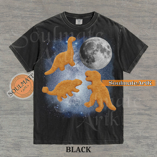 Vintage-style graphic of three golden dinosaur nuggets floating in a blue space nebula with a large moon on a washed black t-shirt.