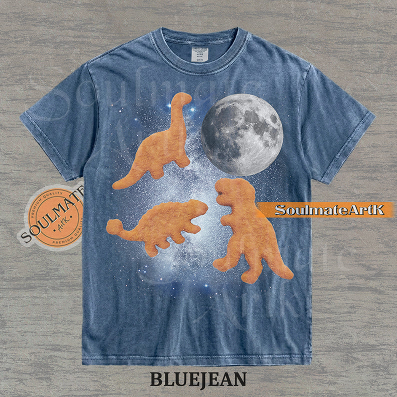 Vintage-style graphic of three golden dinosaur nuggets floating in a blue space nebula with a large moon on a washed bluejean t-shirt.