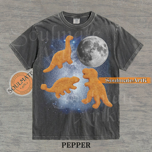 Vintage-style graphic of three golden dinosaur nuggets floating in a blue space nebula with a large moon on a washed pepper t-shirt.