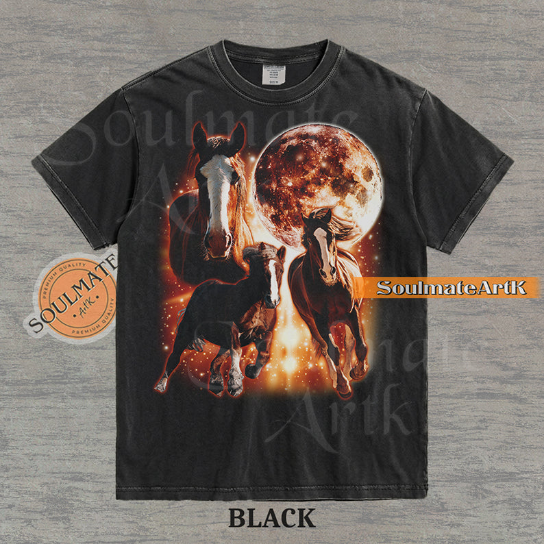 Epic celestial graphic of three horses galloping in front of a giant fiery moon and orange stardust on a washed Black Comfort Colors t-shirt.