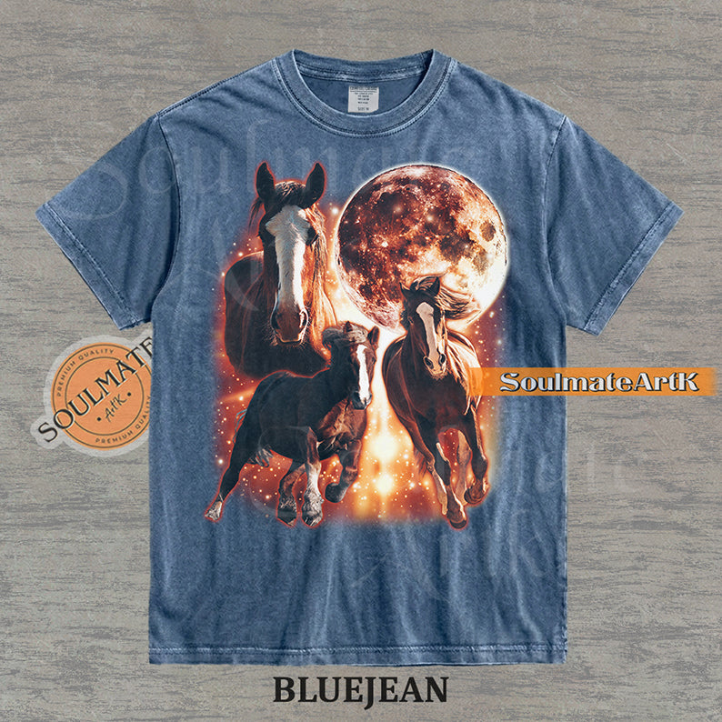 Epic celestial graphic of three horses galloping in front of a giant fiery moon and orange stardust on a washed Blue Jean Comfort Colors t-shirt.