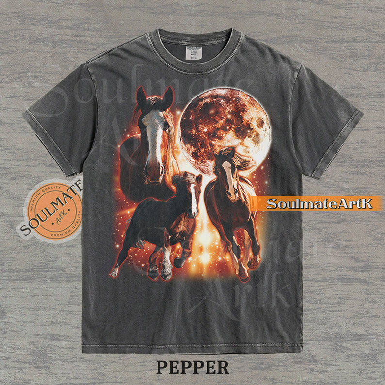 Epic celestial graphic of three horses galloping in front of a giant fiery moon and orange stardust on a washed Pepper Comfort Colors t-shirt.
