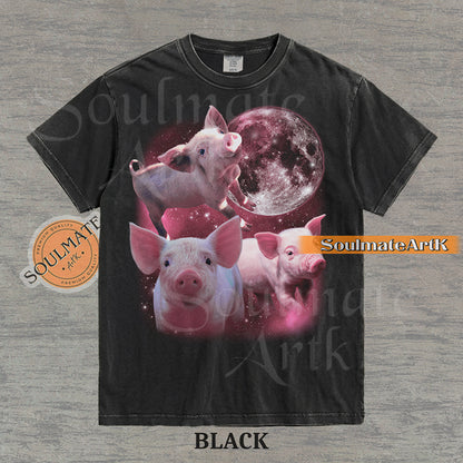 Collage of three pink piglets in front of a glowing pink moon and a starry nebula on a washed black shirt.