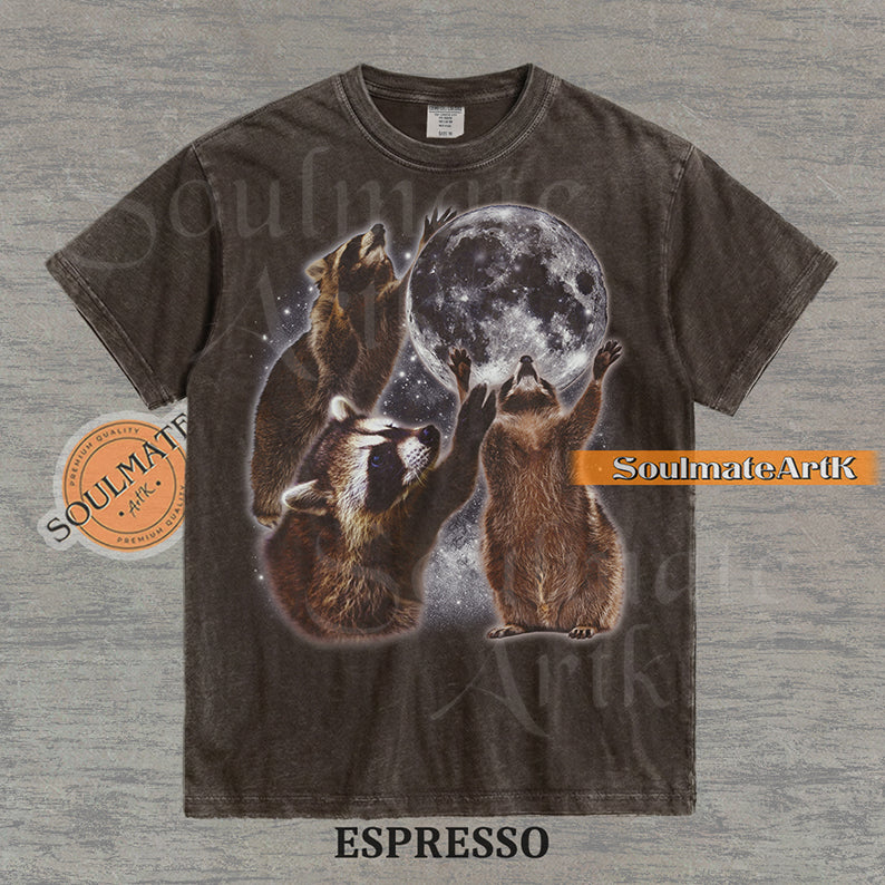Graphic featuring three detailed raccoons reaching for a giant full moon in a starry space setting on a washed Espresso t-shirt.