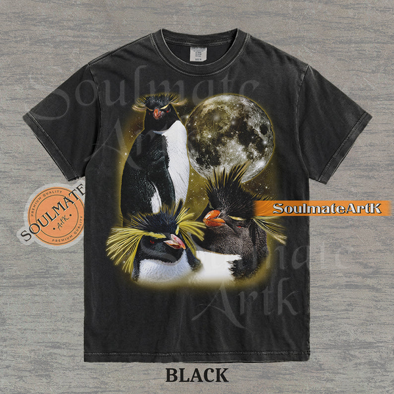 Collage of three Rockhopper penguins with yellow crests in front of a glowing moon and a golden starry nebula on a washed black shirt.