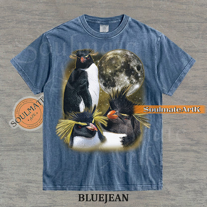 Collage of three Rockhopper penguins with yellow crests in front of a glowing moon and a golden starry nebula on a washed bluejean shirt.
