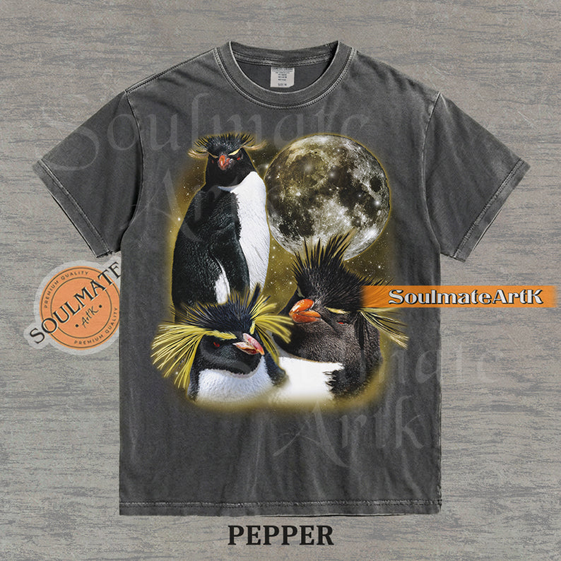 Collage of three Rockhopper penguins with yellow crests in front of a glowing moon and a golden starry nebula on a washed pepper shirt.
