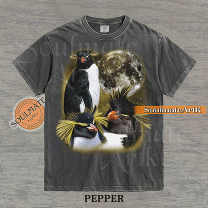 Collage of three Rockhopper penguins with yellow crests in front of a glowing moon and a golden starry nebula on a washed pepper shirt.