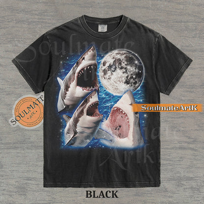 Collage of three great white sharks breaching water in front of a glowing full moon and a starry blue nebula on a washed black shirt.