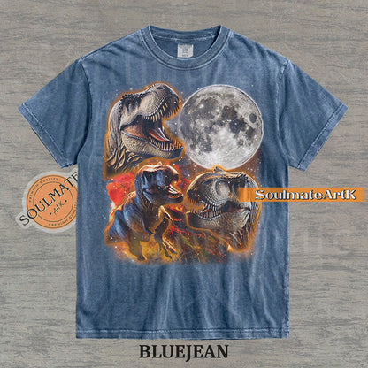 Graphic collage of three T-Rexes next to a large full moon in a starry, colorful space setting on a washed bluejean t-shirt.