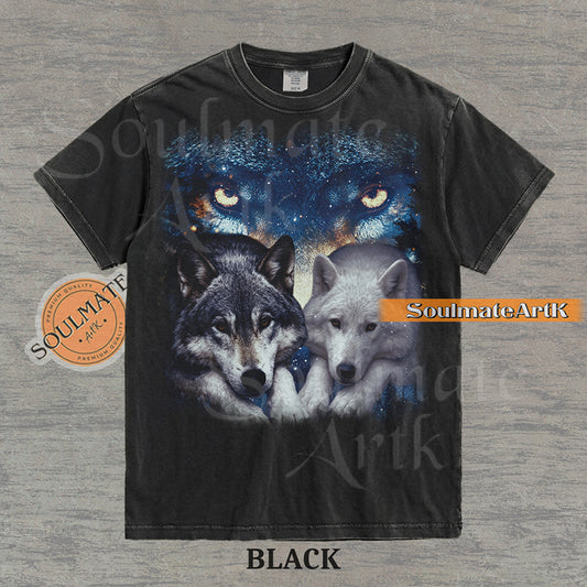 Vintage-style celestial graphic of a timber wolf and arctic wolf resting beneath large glowing wolf eyes in a starry sky on a black t-shirt.