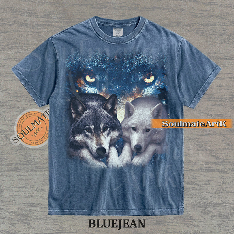 Vintage-style celestial graphic of a timber wolf and arctic wolf resting beneath large glowing wolf eyes in a starry sky on a bluejean t-shirt.