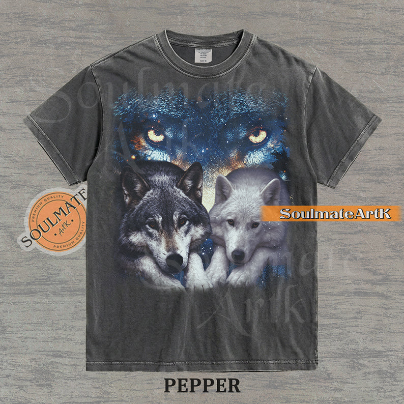 Vintage-style celestial graphic of a timber wolf and arctic wolf resting beneath large glowing wolf eyes in a starry sky on a pepper t-shirt.