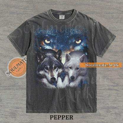 Vintage-style celestial graphic of a timber wolf and arctic wolf resting beneath large glowing wolf eyes in a starry sky on a pepper t-shirt.