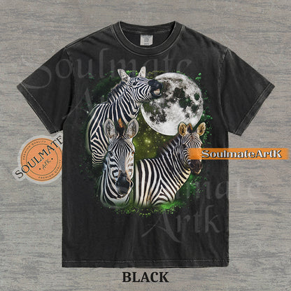Collage of three zebras in front of a glowing white moon and a green starry nebula on a washed black shirt.