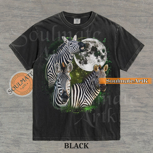Collage of three zebras in front of a glowing white moon and a green starry nebula on a washed black shirt.
