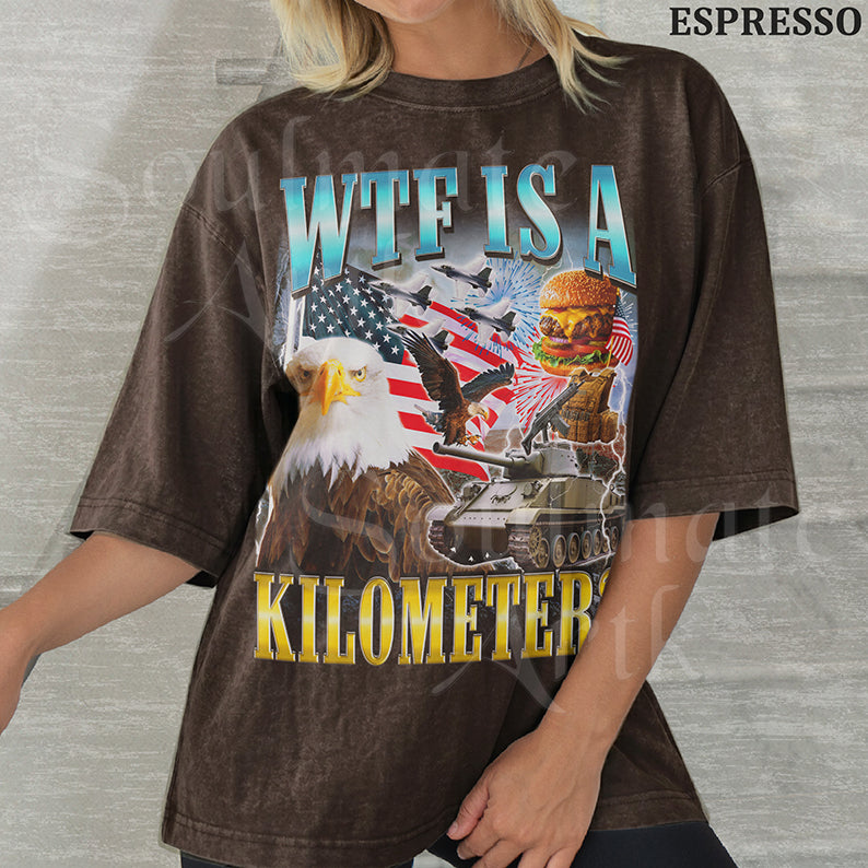 Graphic collage featuring a bald eagle, American flag, fighter jets, a tank, and a burger with bold text reading WTF IS A KILOMETER? on a washed espresso shirt.