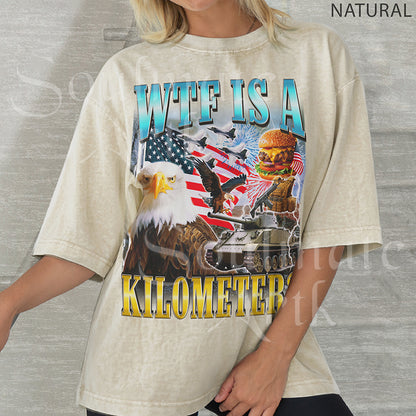 Graphic collage featuring a bald eagle, American flag, fighter jets, a tank, and a burger with bold text reading WTF IS A KILOMETER? on a natural shirt.