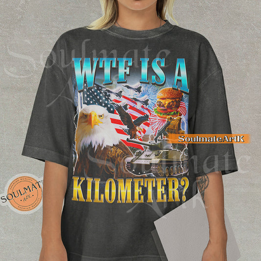 Graphic collage featuring a bald eagle, American flag, fighter jets, a tank, and a burger with bold text reading WTF IS A KILOMETER? on a washed pepper shirt.