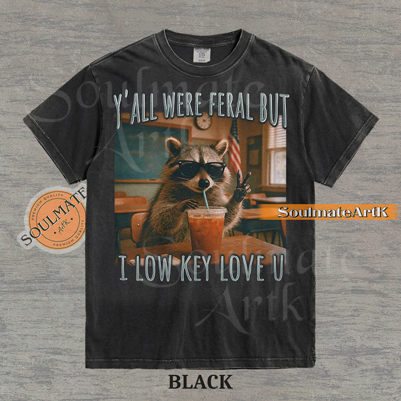 Photorealistic graphic of a raccoon teacher in sunglasses with iced coffee in a classroom under text reading "Y'all Were Feral But I Low Key Love U" on a washed black shirt.